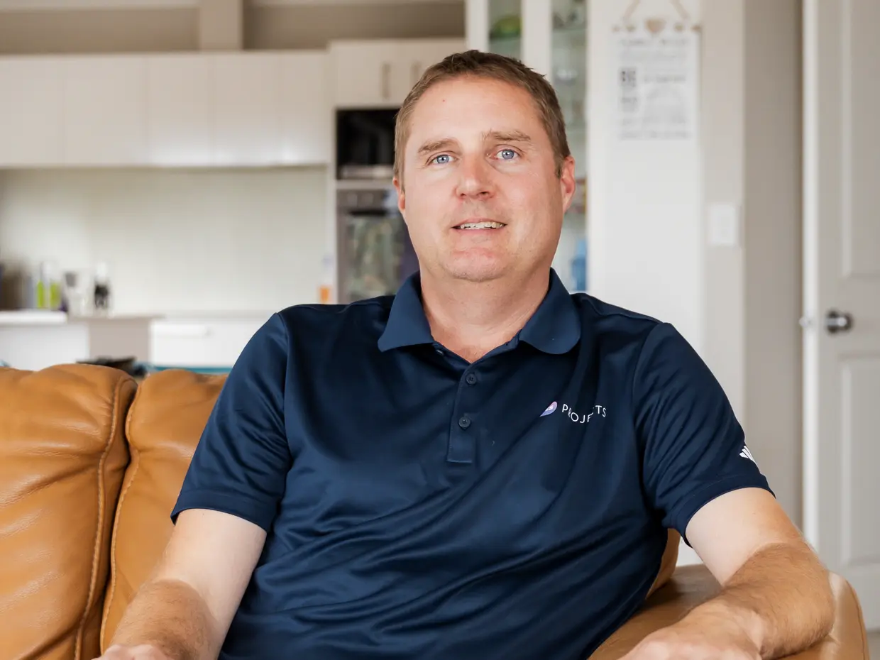 Andy Collis smiling, leaning forward on a sofa with his kitchen behind him