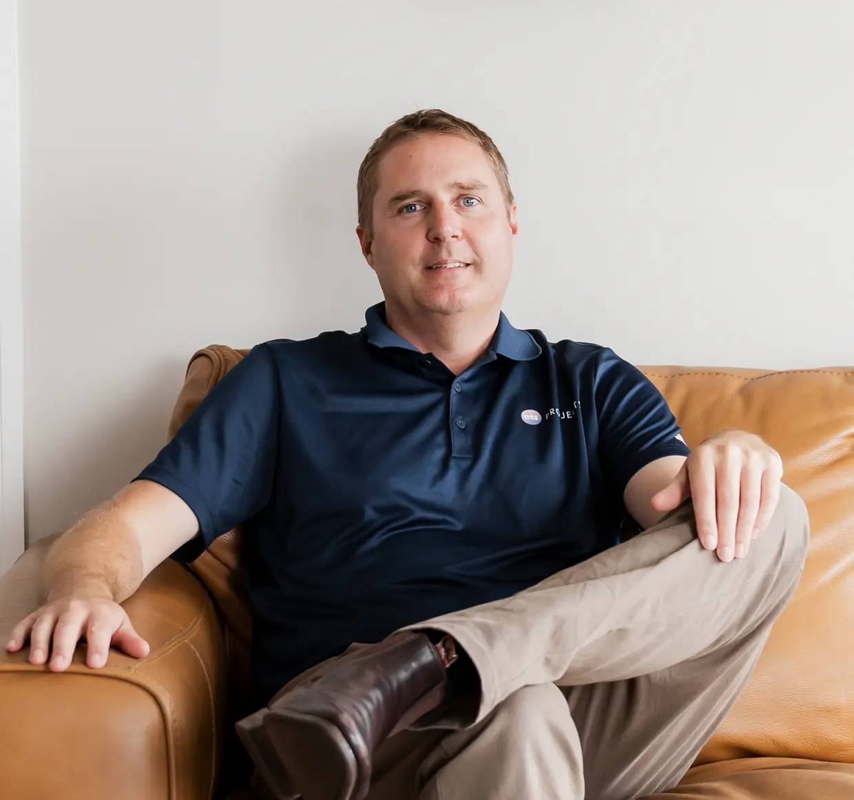 Andy Collis relaxed on a tan leather sofa, one leg crossed